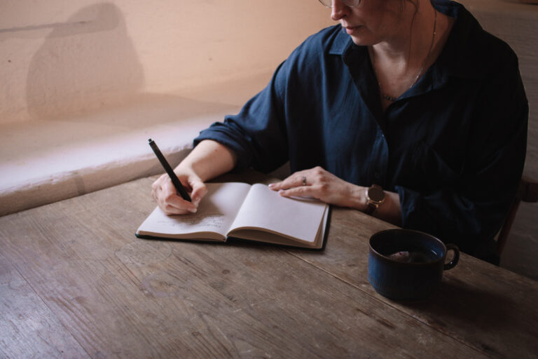 Person sitter vid träbord och skriver i anteckningsbok.