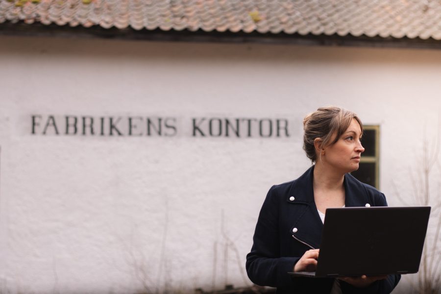 En person håller i en dator och står framför en byggnad med texten Fabrikens kontor på väggen.